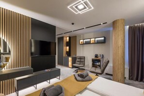 A modern hotel room with a flat-screen TV, a sofa, a bed, a desk, and a chair.