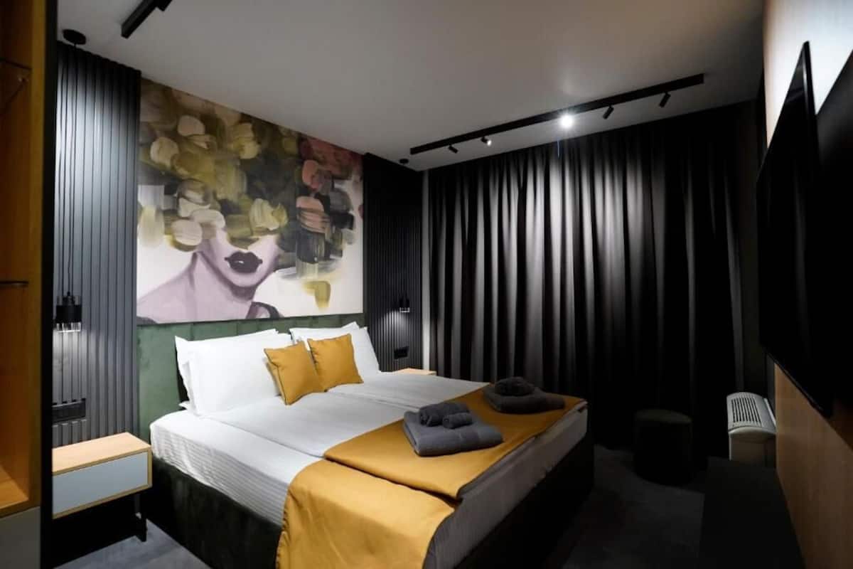 A modern hotel room with a large bed, a painting on the wall, and a TV mounted on the wall.