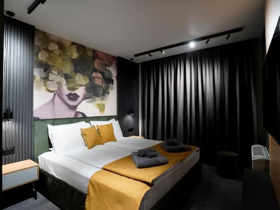 Una habitación de hotel moderna con una cama grande, un cuadro en la pared y un televisor montado.