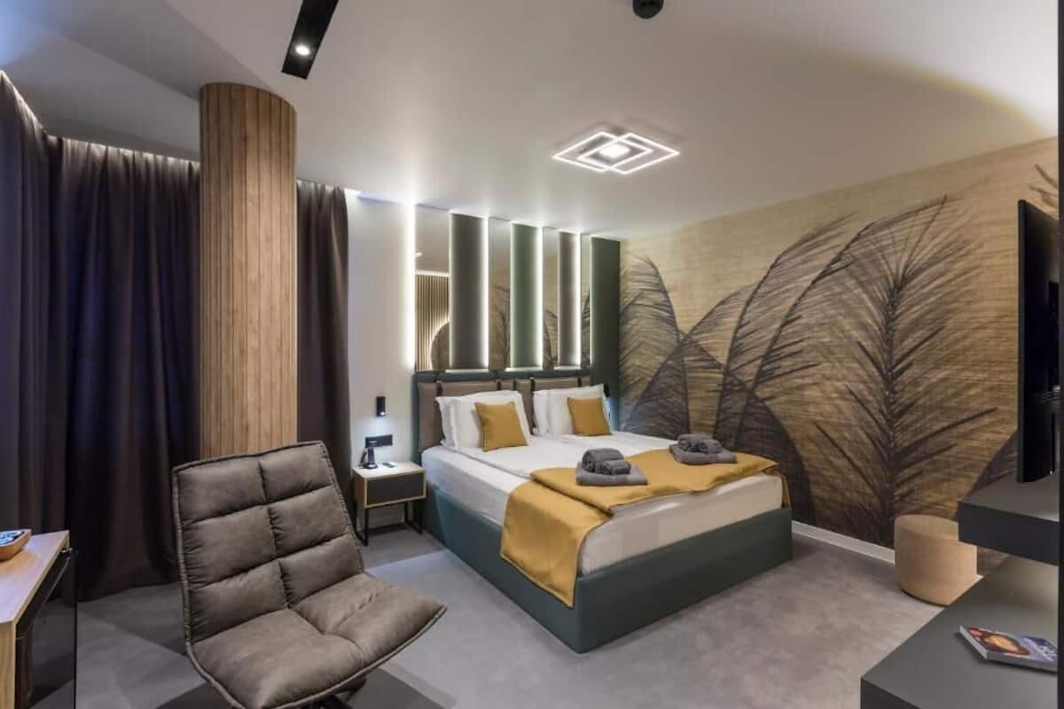 A modern hotel room with a bed, a chair, a desk, and a large wall mural.