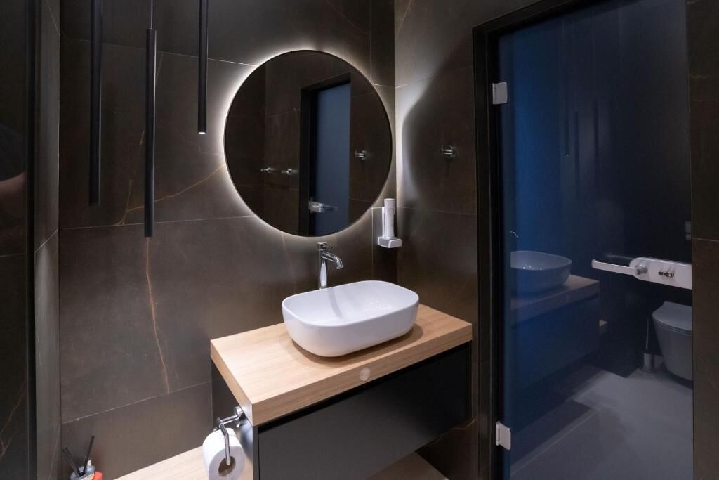 Ein modernes Badezimmer mit rundem Spiegel, weißem Waschbecken und einer Holztischplatte.