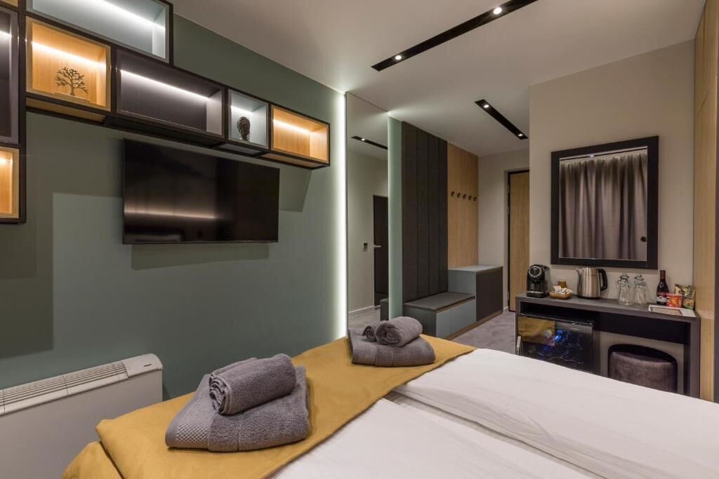 Una habitación de hotel moderna con una cama, un escritorio pequeño con espejo, un televisor y un estante con adornos.