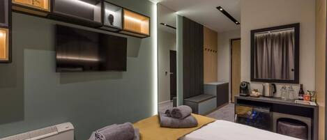 Camera d'albergo moderna con un letto, una piccola scrivania con uno specchio, una televisione e una mensola a parete con oggetti decorativi.