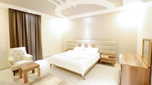 A modern bedroom with a large bed, a chair, a desk, and a mirror. - ALFASWAL ALARBAAH SERVICED APARTMENT  (Taif)