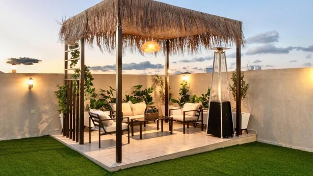 A rooftop patio with a thatched gazebo, outdoor furniture, and ambient lighting. - ALFASWAL ALARBAAH SERVICED APARTMENT  (Taif)