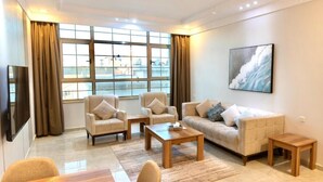 A modern living room with a sofa, armchairs, a coffee table, and a TV. - ALFASWAL ALARBAAH SERVICED APARTMENT  (Taif)