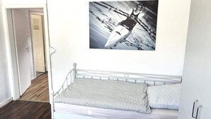 Una cama de metal blanca con ropa de cama a rayas en una habitación con piso de madera y una puerta al fondo.