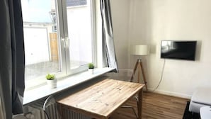 Una habitación con una mesa de madera, un televisor montado en la pared, un radiador y una ventana con cortinas.
