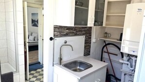 Una cocina compacta con pileta integrada, muebles blancos y salpicadero de piedra.