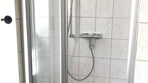 Ducha con cerramiento de vidrio, cabezal de ducha de mano y panel de control en la pared.
