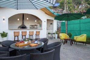 Une terrasse extérieure aménagée avec des meubles en osier, une planche à pizza et un coin bar doté d’un four à pizza.