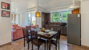 A dining area with a wooden table set for four, a sofa, and a kitchen in the background. - Alaya Stays 2 BHK with Garden & Hill View | Livelife (Kasauli)
