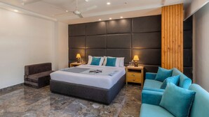 A modern bedroom with a large bed, a wooden accent wall, a ceiling fan, and a blue sofa. - Alaya Stays 2 BHK with Garden & Hill View | Livelife (Kasauli)