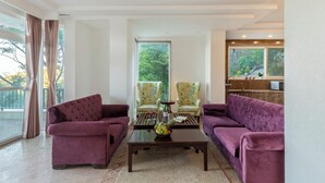 A living room with two purple sofas, a coffee table with fruit, and two patterned armchairs. - Alaya Stays 2 BHK with Garden & Hill View | Livelife (Kasauli)