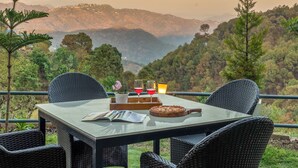 An outdoor dining area with wicker chairs, a table with a pan, and a fire pit. - Alaya Stays 1 BHK with Balcony & Breathtaking View | Baljees Melville Divine (Shimla)