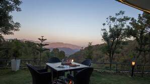 An outdoor dining area with a table and chairs, surrounded by a railing, overlooking a mountainous landscape. - Alaya Stays 1 BHK with Balcony & Breathtaking View | Baljees Melville Divine (Shimla)