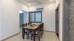 A dining area with a table set for four, a ceiling fan, and an air conditioning unit. - Alaya Stays with Balcony & Hill View | Lake City Heights (Udaipur)