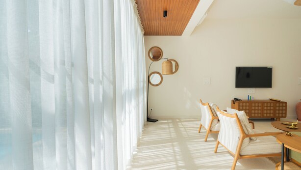 A modern living room with a large window, a flat-screen TV, a wooden cabinet, and two armchairs. - ELIVAAS Mirai Leo | 3 BHK Villa Near Vagator Beach With Pool (Vagator)
