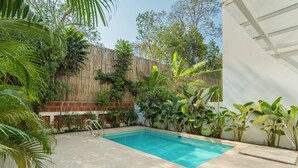 A rectangular swimming pool with a wooden fence and lush greenery surrounding it. - ELIVAAS Mirai Leo | 3 BHK Villa Near Vagator Beach With Pool (Vagator)