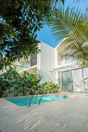 A modern building with a swimming pool, surrounded by lush greenery. - ELIVAAS Mirai Leo | 3 BHK Villa Near Vagator Beach With Pool (Vagator)