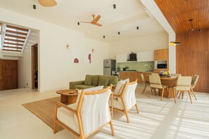 A modern living room with a sofa, chairs, a dining table, and a kitchen in the background. - ELIVAAS Mirai Leo | 3 BHK Villa Near Vagator Beach With Pool (Vagator)