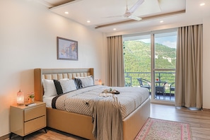 Une chambre dotée d’un grand lit, d’une table de chevet, d’un ventilateur de plafond, d’une fenêtre avec des rideaux et d’un balcon aménagé avec du mobilier d’extérieur.
