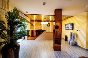 A modern hotel lobby with a wooden reception desk, a large potted plant, a staircase, and a wall-mounted television. - Atlantis Hotels & Apartment (Port Harcourt)