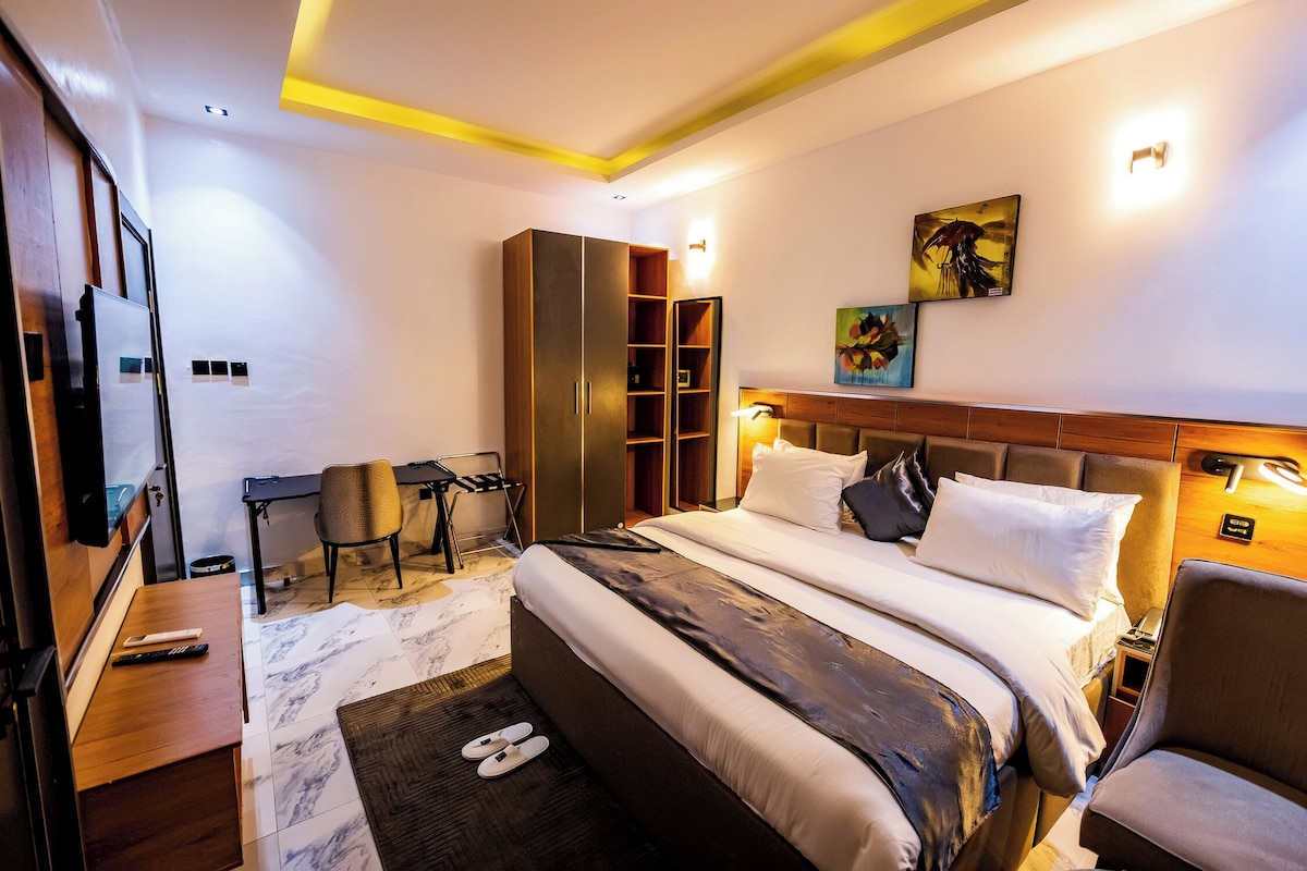 A hotel room with a bed, a desk, a chair, a wardrobe, and artwork on the wall.