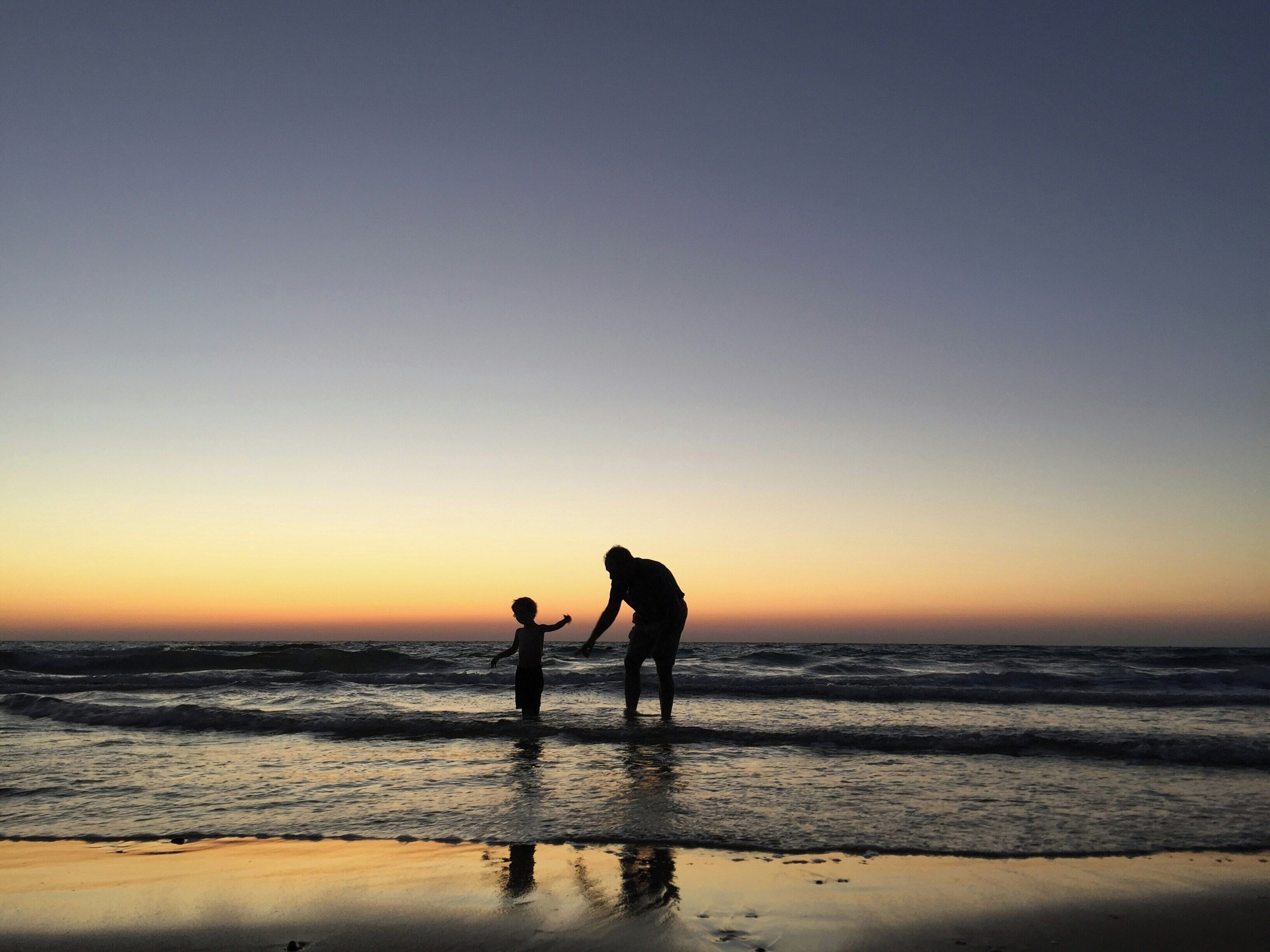 A silhouette of a person and a child at the beach during sunset.