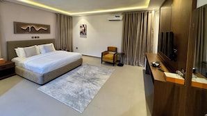 A modern hotel room with a large bed, a seating area, a TV, and a minibar. - LUMAANA RESIDENCES (Abuja)