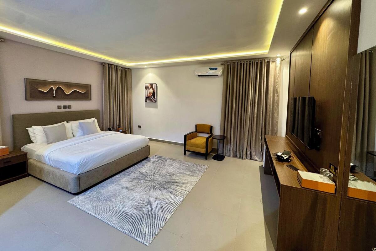 A modern hotel room with a large bed, a seating area, a TV, and a minibar.