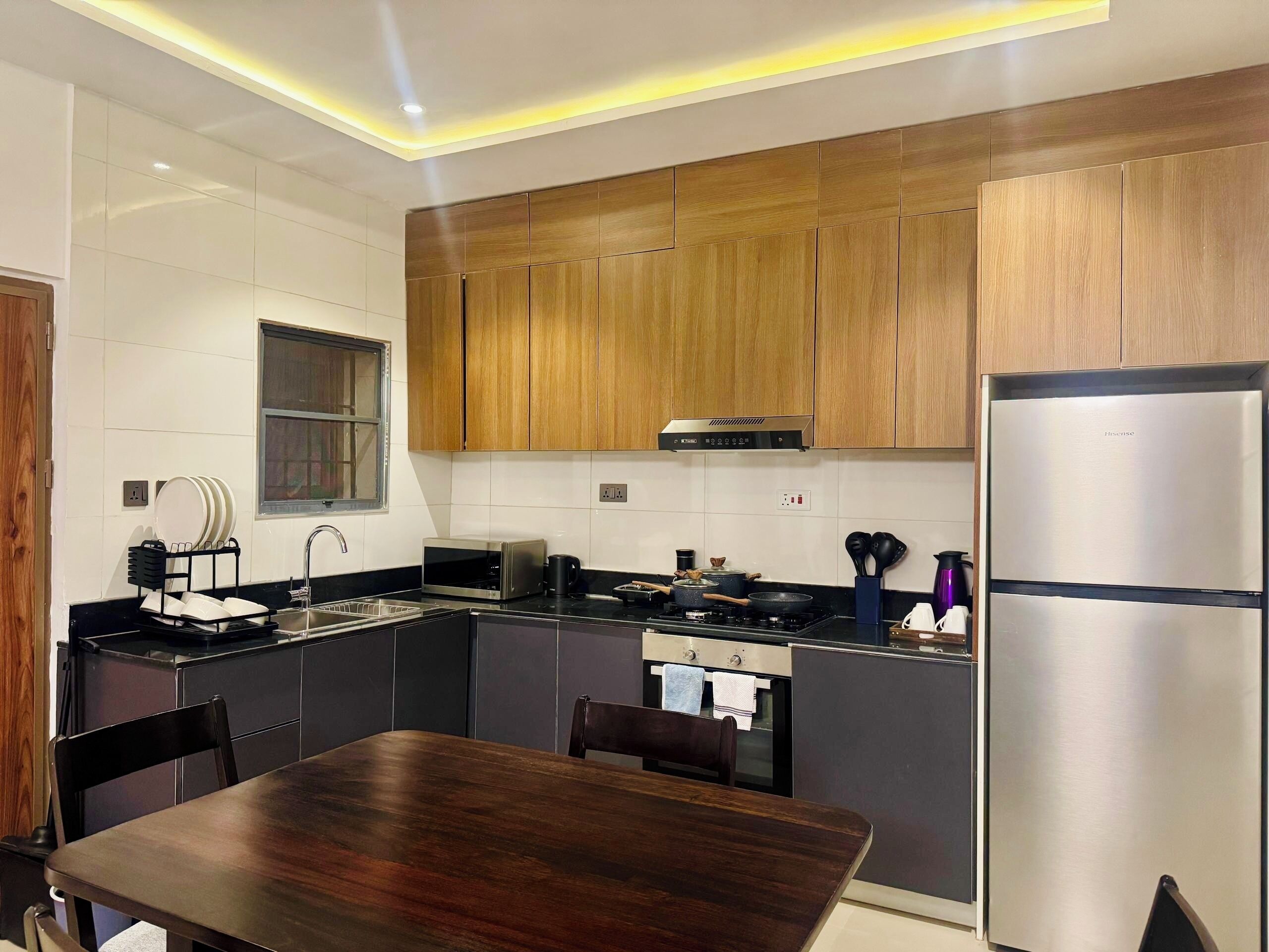 A modern kitchen with wooden cabinets, a stainless steel refrigerator, and a dining table.