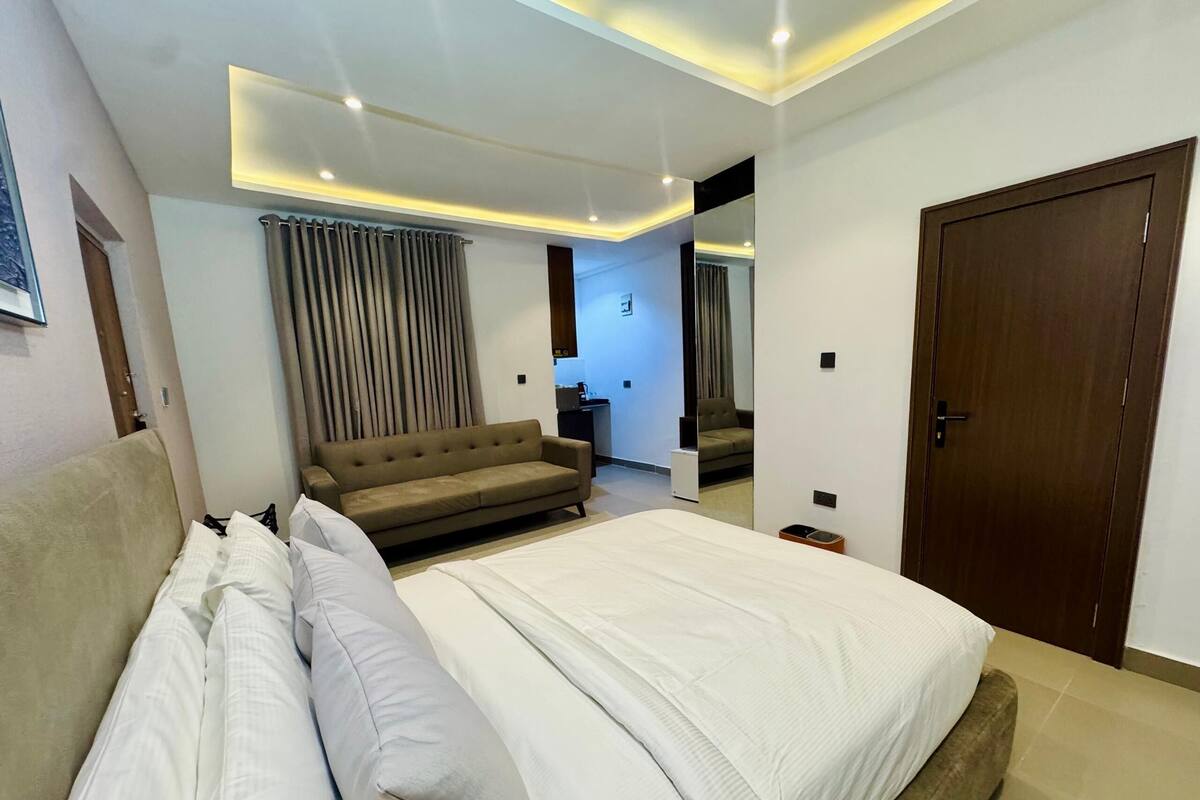 A modern bedroom with a large bed, a sofa, and a mirror.