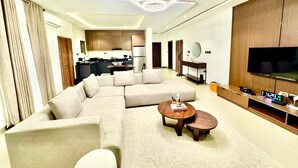 A modern living room with a sectional sofa, a round coffee table, and a flat-screen TV. - LUMAANA RESIDENCES (Abuja)