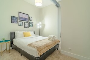 A neatly made bed with a white comforter, a yellow pillow, and a folded towel on the side. There are framed pictures on the wall above the bed. - Chicago Spacious 3Br Smoke Ok Near McCormick Place (Chicago)
