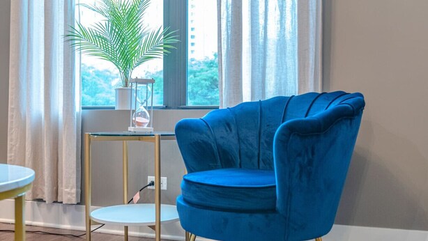 A blue armchair with gold legs, a small round table, and a potted plant on a glass table beside a window with curtains. - Chicago Spacious 3Br Smoke Ok Near McCormick Place (Chicago)