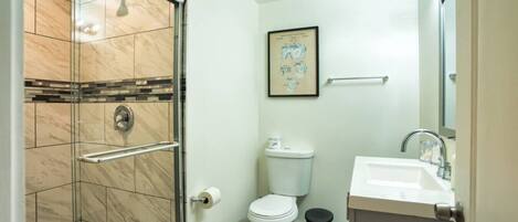 Une salle de bain avec une douche à parois de verre, des toilettes, un lavabo et un tableau encadré au mur.