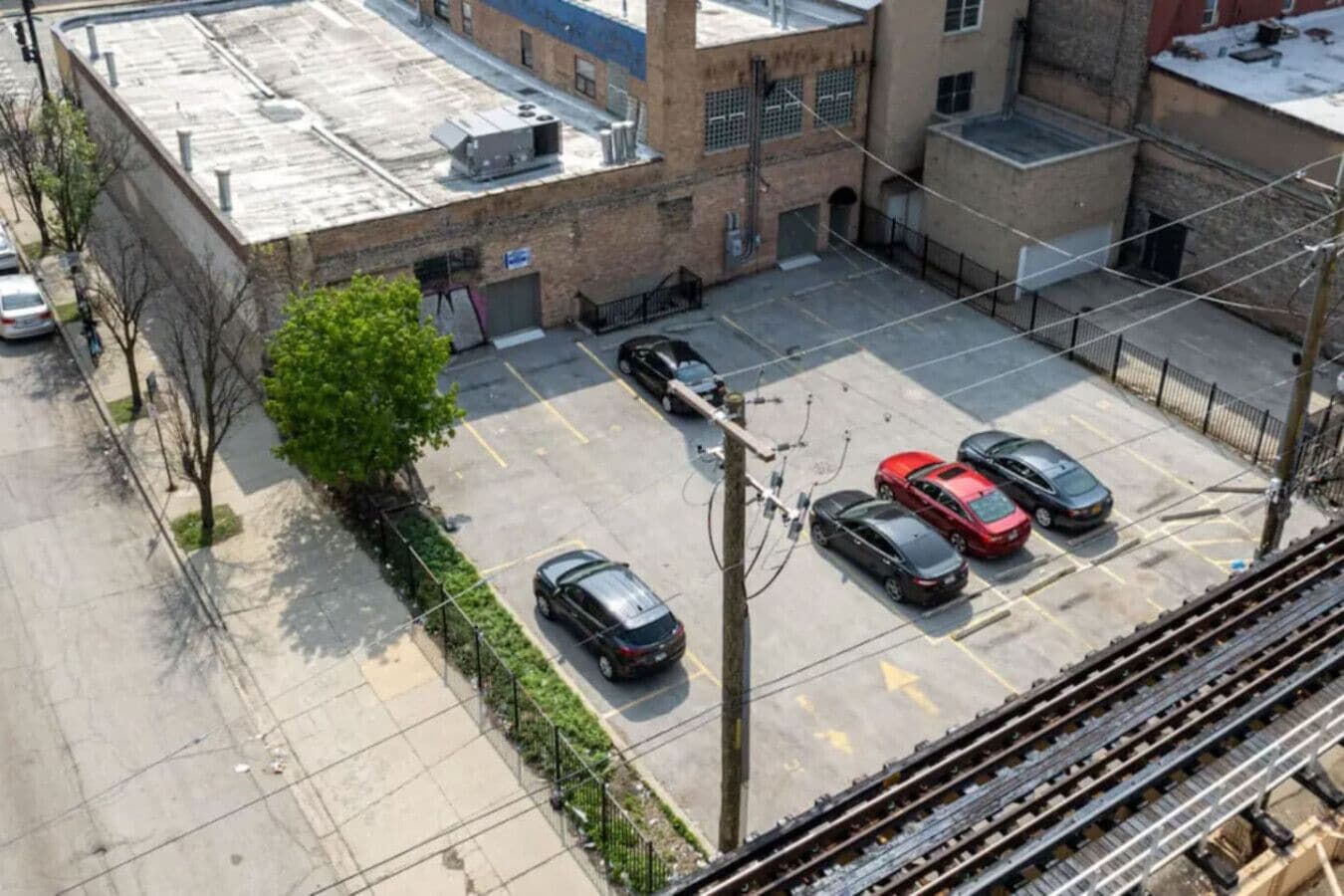 Ein Luftbild eines Parkplatzes mit mehreren Autos, einem Baum und einem Gebäude mit Backsteinfassade.