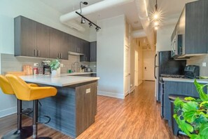A modern kitchen with dark cabinets, a central island, and a yellow bar stool. - Stylish friendly 3BR Suite near McCormick (Chicago)