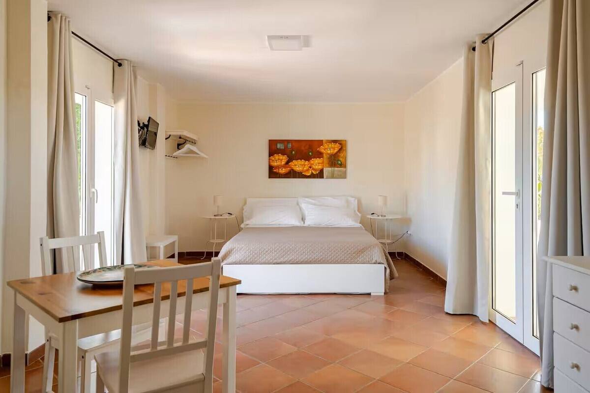 A bedroom with a bed, a bedside table, a chair, a small table, and a painting on the wall.