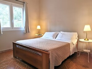 A neatly made bed with white linens, two bedside lamps, and a window with curtains. - Villa Mar (Noto)