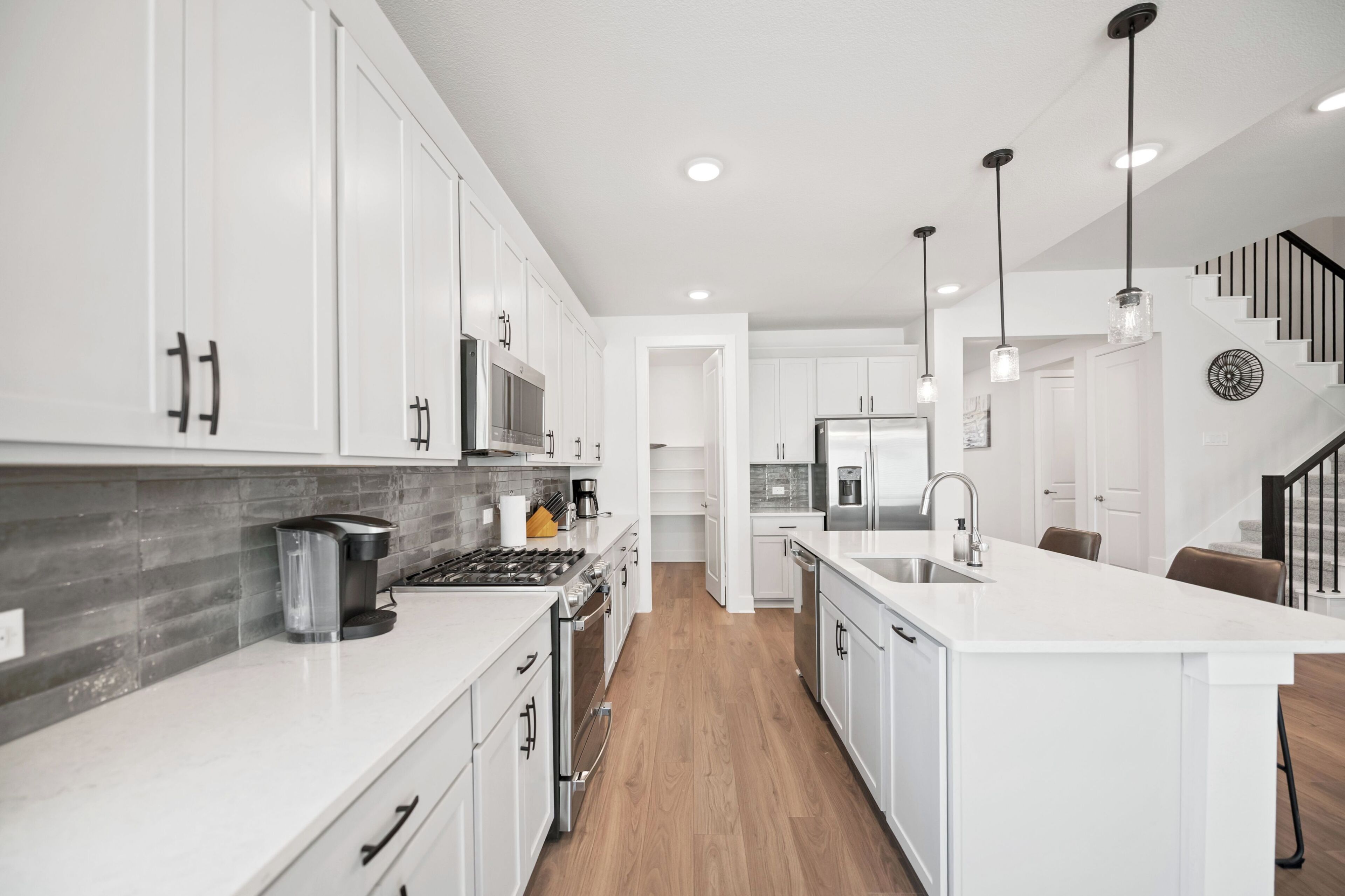 A modern kitchen with white cabinetry, stainless steel appliances, and a wooden floor.