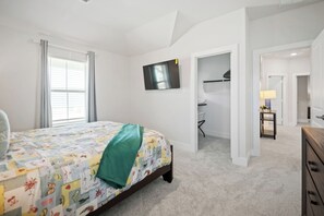 Ein Schlafzimmer mit einem Bett, einem an der Wand befestigten Fernseher und einem Schreibtisch mit Stuhl.