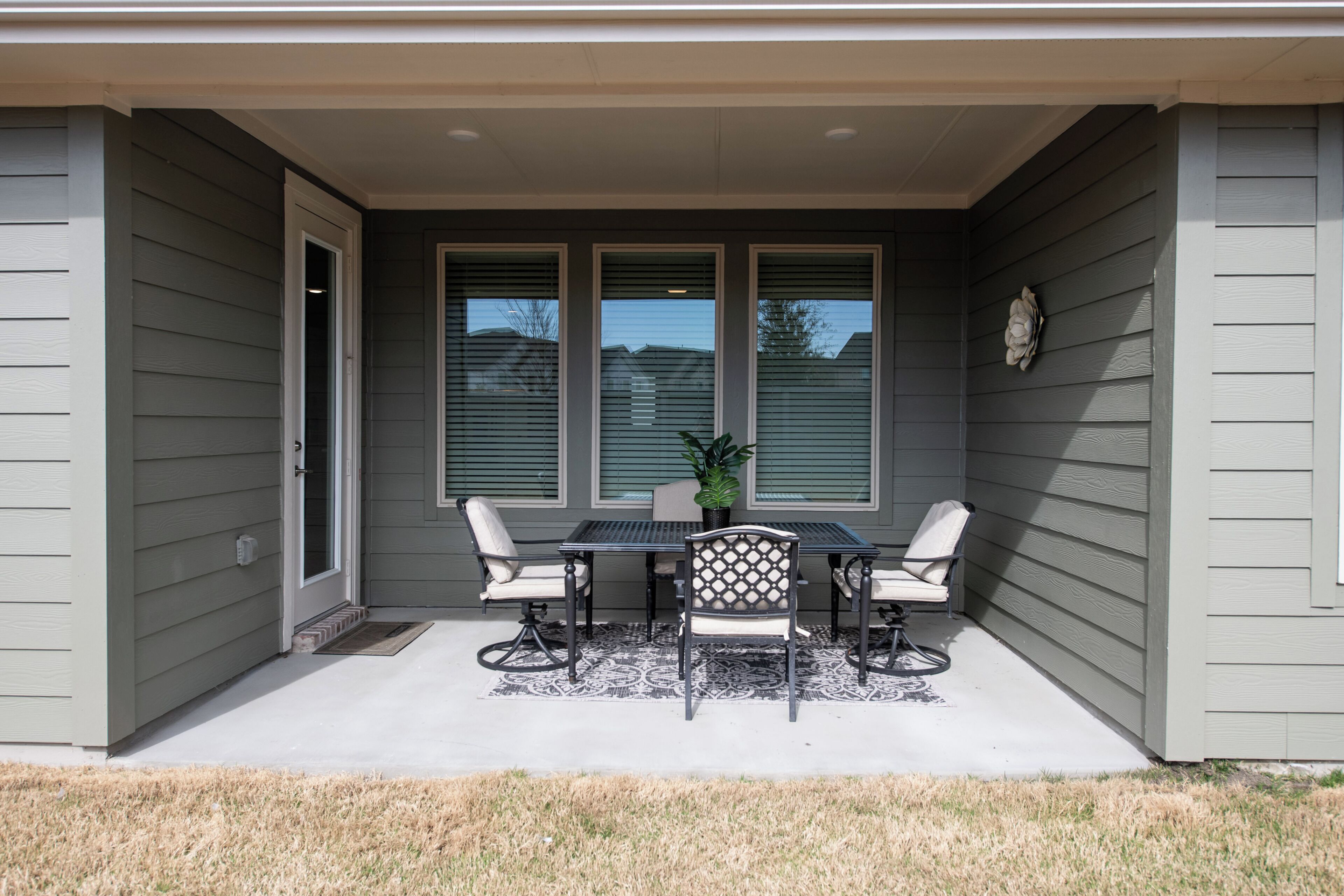 A covered patio with a table and four chairs, a potted plant, and a decorative wall piece.