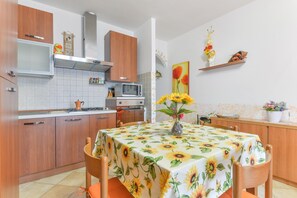 Een keuken met houten kastjes, een magnetron en een eettafel met een tafelkleed met zonnebloemen.