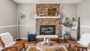 A living room with a brick fireplace, wooden chairs, a round coffee table, and a floor lamp.