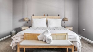 A neatly arranged bedroom with a large bed, two bedside tables, a bench, and two hanging lamps.