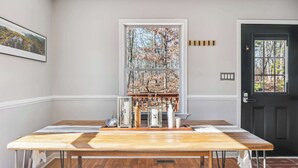 A dining area with a long wooden table, a window with a view of trees, and a black door.