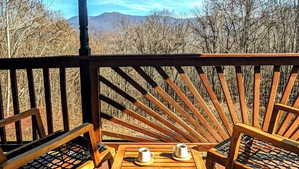 A wooden deck with a table and two chairs, overlooking a mountainous landscape.