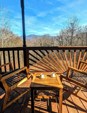 A wooden deck with a table and two chairs, overlooking a mountainous landscape.